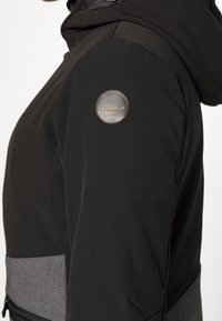 Czarna kurtka z kapturem z szarym akcentem z tkaniny w talii, gładką teksturą i okrągłym metalowym logo na lewym ramieniu.