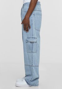 Lyseblå denim cargo-bukser med sidelommer, bred ben-design og sømdetaljer. Bært med hvite joggesko.