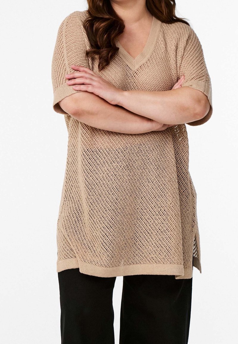 Beige mesh gebreide V-hals top met korte mouwen, met een losse pasvorm en zijsplitten, gecombineerd met zwarte wijde broek.