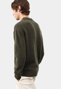 Ciemnozielony sweter z dzianiny z prążkowanymi mankietami i dołem, cechujący się klasycznym okrągłym dekoltem i luźnym krojem. Teksturowany materiał wełniany.