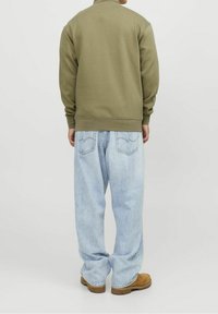 Olivgrön sweatshirt med rund halsringning, ribbade ärmslut och nederkant, i kombination med ljusblå baggy jeans och bruna skor. Enkel, avslappnad stil.