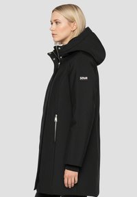 Zwarte waterdichte jas met een hoge kraag, ritssluitingen op de zakken, verstelbare capuchon en een logopatch op de mouw. Gladde textuur en rechte snit.