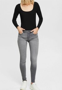 Black ribbed long-sleeve bodysuit paired with gray skinny jeans. The jeans feature a classic five-pocket design and a fitted silhouette. White sneakers complete the outfit.