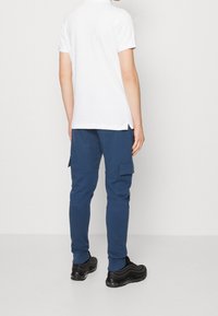 Biała koszulka polo z krótkim rękawem w połączeniu z niebieskimi joggerami cargo z bocznymi kieszeniami, teksturowanym materiałem oraz czarnymi sneakersami o gładkim wykończeniu.