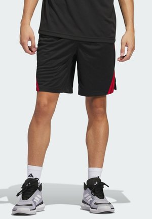 Person wearing black athletic shorts with red side stripes, white crew socks, and gray and black Adidas sneakers, standing on a light background.