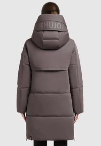 Zateplená parka do délky ke kolenům v tlumené šedé barvě. Obsahuje velkou kapuci, logo značky na zadní straně a elastické manžety. Hladká textura a elegantní design.