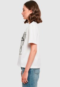 Weißes T-Shirt mit kurzen Ärmeln und einem grafischen Druck auf der Vorderseite, das eine stilisierte schwarze Illustration zeigt. Aus Baumwolle, legere Passform.