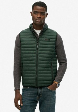 Groene gewatteerde vest met een quiltpatroon, ritsen en zijzakken, gedragen over een grijze, gemêleerde blouse met lange mouwen.