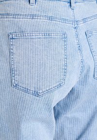 Svetlomodré rifle s vertikálnymi bielymi tenkými prúžkami, vybavené dvoma zadnými vreckami. Tkanina má hladkú textúru s viditeľnými detailmi švov.