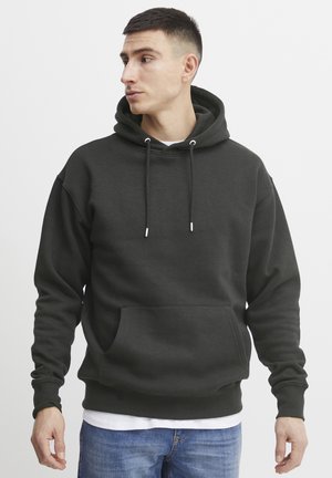 Sudadera de color gris oscuro hecha de tejido suave. Presenta un bolsillo estilo canguro, capucha con cordón ajustable y puños acanalados. Lleva encima una camiseta blanca.