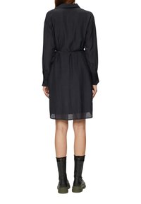 Dunkelgraues Hemdkleid mit langen Ärmeln, Kragen, tailliertem Bund und durchscheinendem unteren Saum, getragen mit schwarzen Stiefeln und olivgrünen Sohlen.