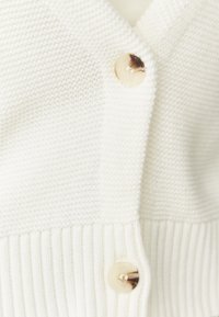 Cardigan bianco lavorato a maglia con un corpo texturizzato, orlo a coste e bottoni rotondi di colore chiaro.