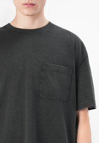 Dark grey short-sleeve t-shirt made of cotton, featuring a chest pocket, ribbed crew neckline, and a relaxed fit. Smooth texture.