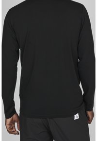 Svart långärmad skjorta i mjukt material, med en enkel, slät textur och utan synliga mönster. Har en liten etikett i fållen.