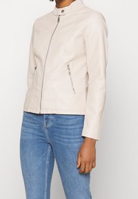 Jasnobeżowa skórzana kurtka ze stójką, z przodu zapinana na zamek błyskawiczny, z dwoma zapinanymi na zamek bocznymi kieszeniami. Gładka faktura i dopasowany krój.
