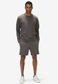 Grå bomullströja med lång ärm, rund halsringning och matchande gråa shorts. Modellen bär vita sneakers och visar upp en avslappnad passform.