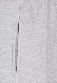 Helehall kangas, millesse on õmmeldud vertikaalne lõhikuga tasku, mis näitab pehmet, tekstuurset kudumit lähiplaanis.