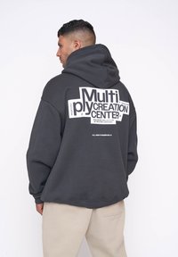 Sudadera negra de gran tamaño con un gran gráfico blanco en la parte posterior, que incluye texto y un símbolo de marca registrada. Puños y dobladillo acanalados.