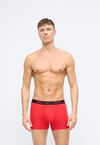 Červené boxerky z elastického materiálu s čiernym elastickým pásom, na ktorom je biele logo "NIKE". Ohraničujúci dizajn, hladká textúra.