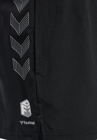 Pantalones cortos deportivos negros con una textura suave, un patrón de rayas en forma de chevron en blanco diagonal y un logo en la parte inferior izquierda.