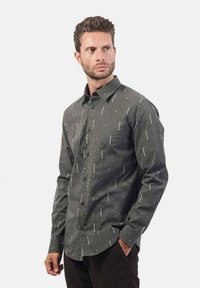 Camicia con bottone in grigio scuro con righe verticali e accenti bianchi sparsi. Maniche lunghe e colletto classico, vestibilità sagomata, texture liscia.