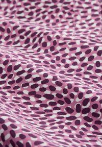 Stoffe mit einem rosa Hintergrund, die ein Muster aus dunkelvioletten und weißen abstrakten Formen zeigen und eine strukturierte Optik erzeugen.