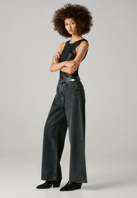 Melnā bezpiedurkņu blūze ar spīdīgu tekstūru; brīvi pieguļošas tumšas džinsas ar izkaisītiem rotājumiem; melni zābaki ar papēdi līdz potītei.