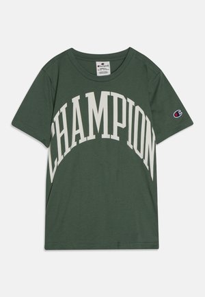 Zielona koszulka Champion z krótkim rękawem, z dużym białym, zakrzywionym napisem „CHAMPION” z przodu i małym haftowanym logo na lewym rękawie.