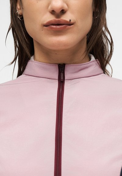 Ανοιχτό ροζ τζάκετ με φερμουάρ και ψηλό γιακά. Διαθέτει μαβιοκόκκινο φερμουάρ και λείο υλικό, σχεδιασμένο για εφαρμοστή εμφάνιση.