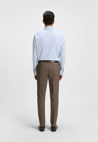 Camicia azzurra chiara con maniche lunghe e colletto a punte, abbinata a pantaloni marroni su misura. Tessuto morbido, vestibilità slim, design classico.