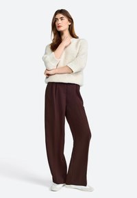 Maglione cremoso e peloso con polsini a coste, abbinato a pantaloni larghi marroni e scarpe chiare, per un look rilassato.