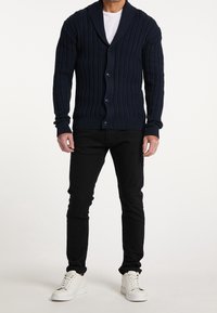 Námořnický žebrovaný cardigan s šálovým límcem, pěti knoflíky a dlouhými rukávy, spárován s černými kalhotami a bílými teniskami.