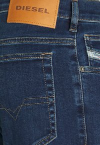 Dunkelblaue Jeans aus Denim mit einem Lederetikett von DIESEL am Bund. Verfügt über klassische Taschenstickereien und sichtbare Nähte.