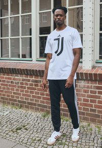 Balta t-kreklu ar melnu Juventus logotipu, kombinēts ar melnām sporta biksēm ar baltām sānu svītrām. Apavi ir balti ar sarkaniem akcentiem.