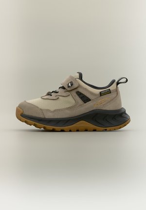 Beige og tan vandtæt vandresko med sort sål, velcrolukning og trækkemærke ved hælen vist i sideprofil.
