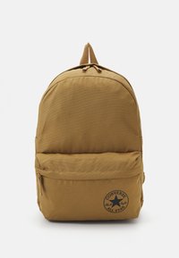 Zaino beige realizzato in tessuto resistente, con una parte superiore tondeggiante, tasca frontale con zip e un dettaglio con logo circolare nella parte inferiore.
