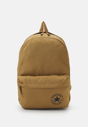 Zaino beige realizzato in tessuto resistente, con una parte superiore tondeggiante, tasca frontale con zip e un dettaglio con logo circolare nella parte inferiore.
