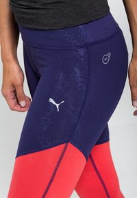 Marinblå och röda träningsleggings med en texturerad mönster, kontrasterande färgblock, Puma-logotyp och detaljer om fukttransporterande teknik.