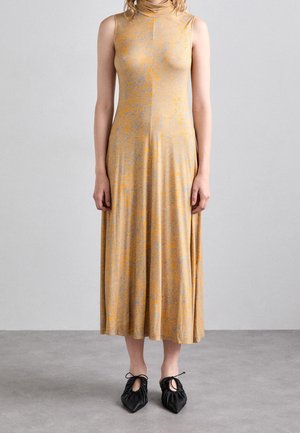 Robe sans manches, longue jusqu'au sol, de couleur orange clair avec des motifs bleus subtils. Associée à des chaussures noires souples et plissées avec des détails découpés.