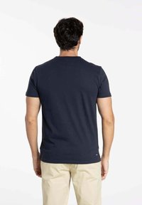 T-shirt en coton bleu marine à manches courtes, col rond, avec un accent de logo subtil sur l'ourlet inférieur. Texture lisse, design ajusté.