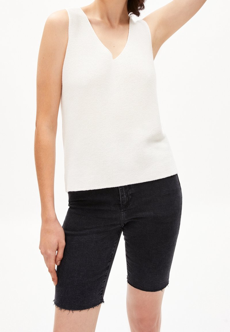Haut sans manches blanc texturé avec un col en V, associé à un short en denim foncé aux bords effilochés. Design simple et ajusté.