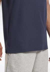 Námorně modré bavlněné tričko s texturovaným povrchem, s postranními rozparky. V kombinaci se světle šedými tepláky, které mají měkkou texturu látky.
