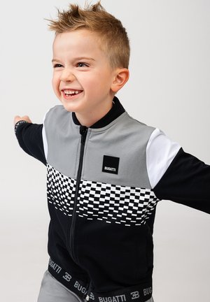 Black and grey zip-up jacket featuring a checkerboard pattern across the chest, with white shoulder accents and branded waistband.