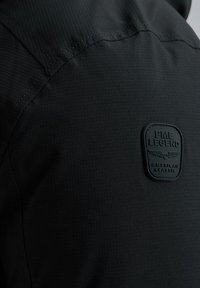 Schwarze strukturiertes Jackett mit einem kleinen rechteckigen Patch, auf dem "PME LEGEND" und "AMERICAN CLASSIC" in einer kontrastierenden Farbe geprägt sind.
