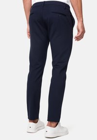 Granatowe dopasowane spodnie o gładkiej fakturze i dwóch tylnych kieszeniach; zestawione z białymi sneakersami.