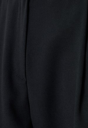 Primer plano de una tela negra, con una textura suave y un diseño ligeramente drapeado. Los detalles de costura visibles añaden un carácter sutil.