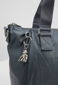 Sac à main en tissu gris foncé avec des poignées larges et un petit porte-clés argenté brillant en forme d'ours fixé près de la fermeture éclair.
