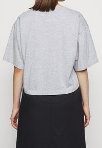 Grå kortärmad t-shirt i mjuk bomullsblandning, med rund halsringning, kombinerad med en svart kjol. Minimalistisk design.