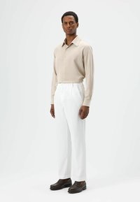 Beige overhemd met knopen, witte broek met fijne strepen, bruine loafers. Slanke pasvorm, gladde textuur en op maat gemaakt ontwerp, met een klassieke kraag.