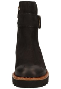 Bottine noire en cuir avec une sangle à boucle, semelle épaisse et bordure cousue marron, vue de face.